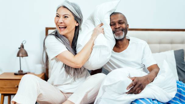 Casal feliz na cama, brincando com travesseiros após acordar